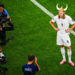 Erling Haaland má na sebe vikingskú prilbu a bielu uniformu, keď pózuje na ihrisku pre fotografov
