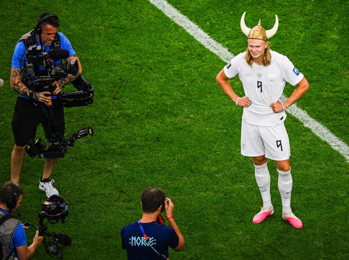 Erling Haaland má na sebe vikingskú prilbu a bielu uniformu, keď pózuje na ihrisku pre fotografov