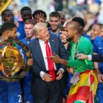 Reece James dvíha trofej z majstrovstiev sveta klubov FIFA na pódiu s Donaldom Trumpom neďaleko.