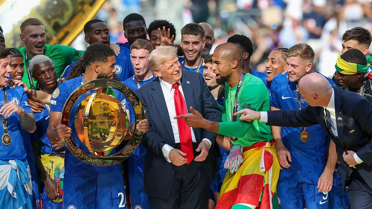Reece James dvíha trofej z majstrovstiev sveta klubov FIFA na pódiu s Donaldom Trumpom neďaleko.