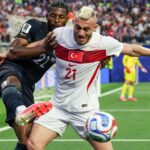 Futbalista v čiernej uniforme kopne nohou smerom k lopte, ktorá je pred hráčom v bielo-červenej uniforme.