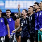 Skupina športovcov oblečených v modrých a čiernych uniformách, možno futbalisti, stojí tesne vedľa seba na ihrisku.